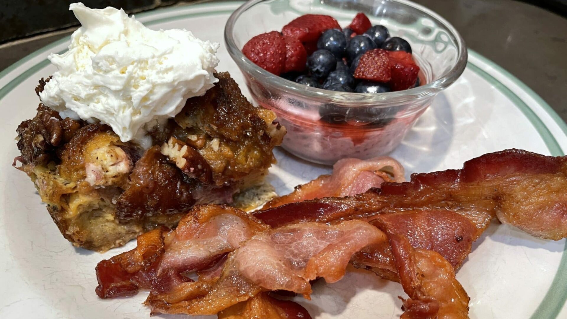 Blueberry Croissant French Toast on a white plate with fruit and bacon