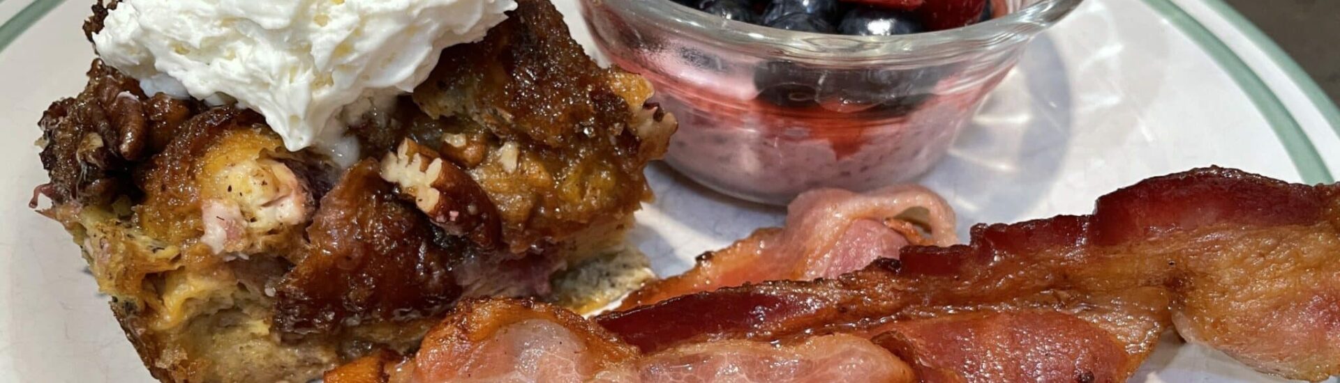 Blueberry Croissant French Toast on a white plate with fruit and bacon