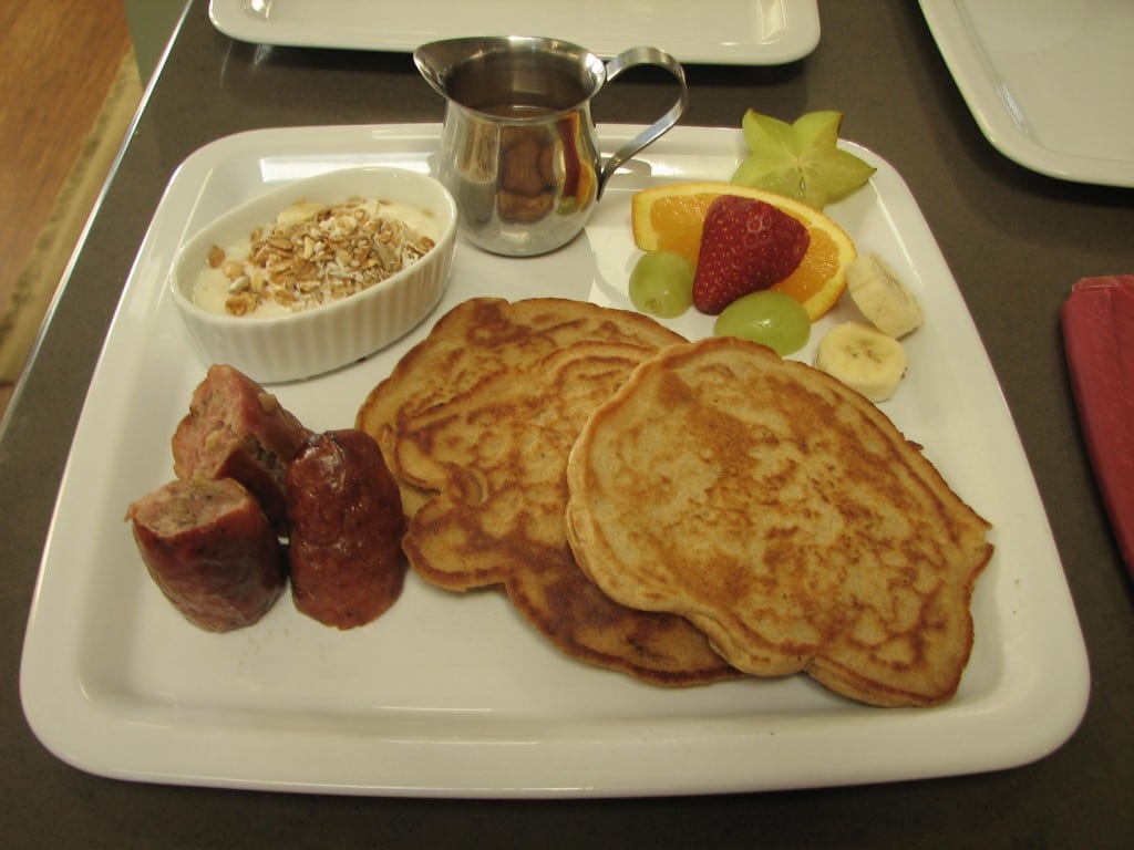 Apple Pancakes on a square white plate with sausage, fresh fruit and yogurt