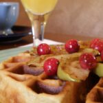 Warm hazelnut waffle with apples and currants and a glass of orange juice