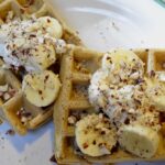 Hazelnut Waffles on a white plate with whipped cream and bananas