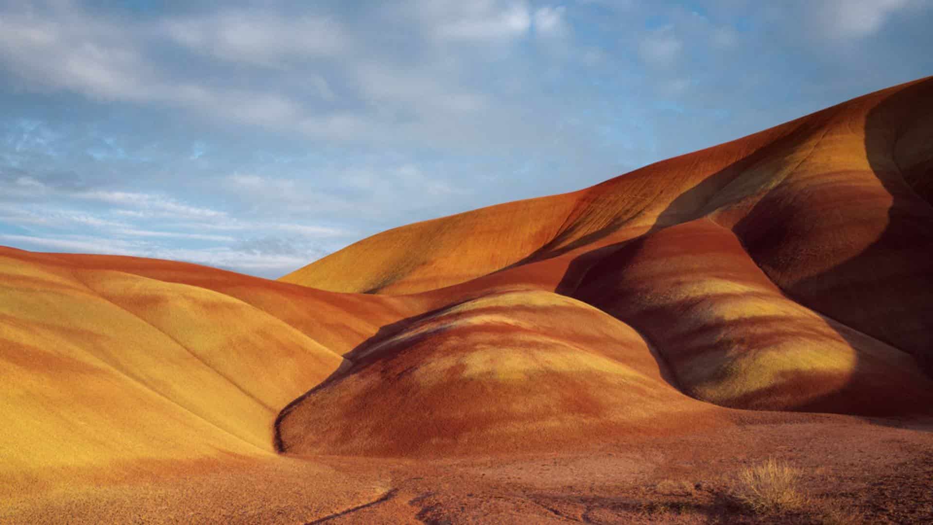 Large orange and yellow sand dunes with blue and gray sky in the background