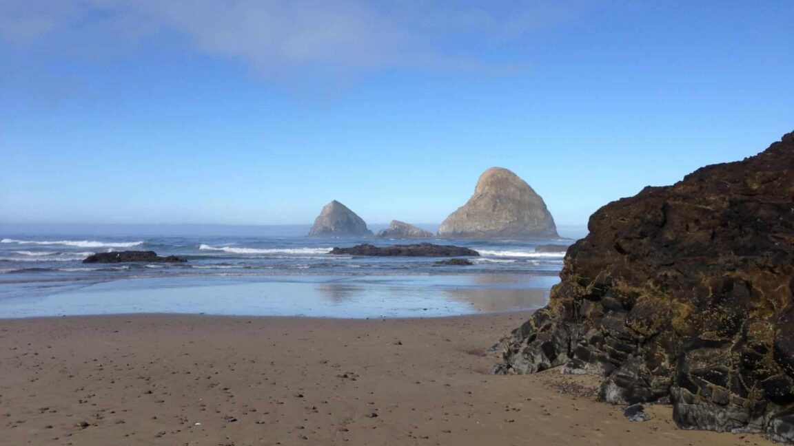 Wet sandy beach with soft rolling waves and three very large rocks in the protruding through the water