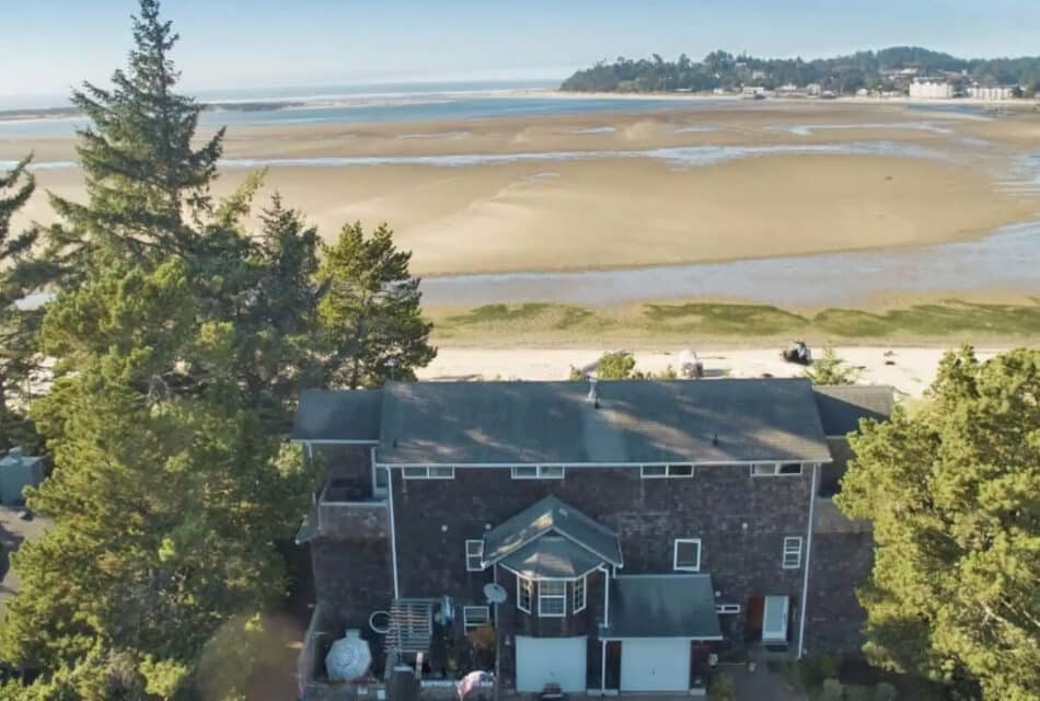 Aerial view of property surrounded by green trees and located near a beach and water