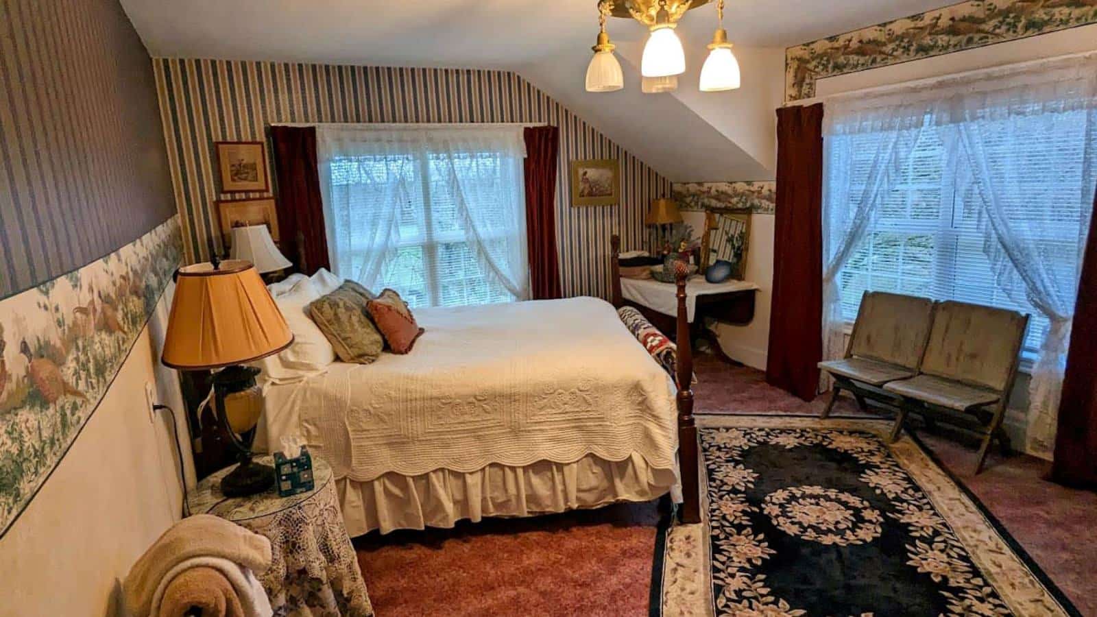 Bedroom with white walls, pheasant and striped wallpaper, carpeting, wooden four poster bed, white bedding, and large windows