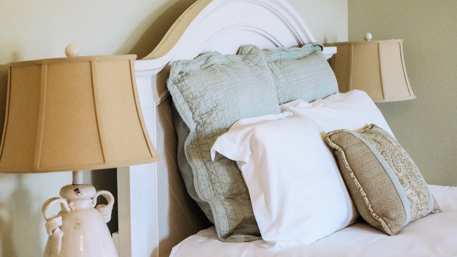 Close up view of white headboard, multicolored pillows, white bedding, and lamps