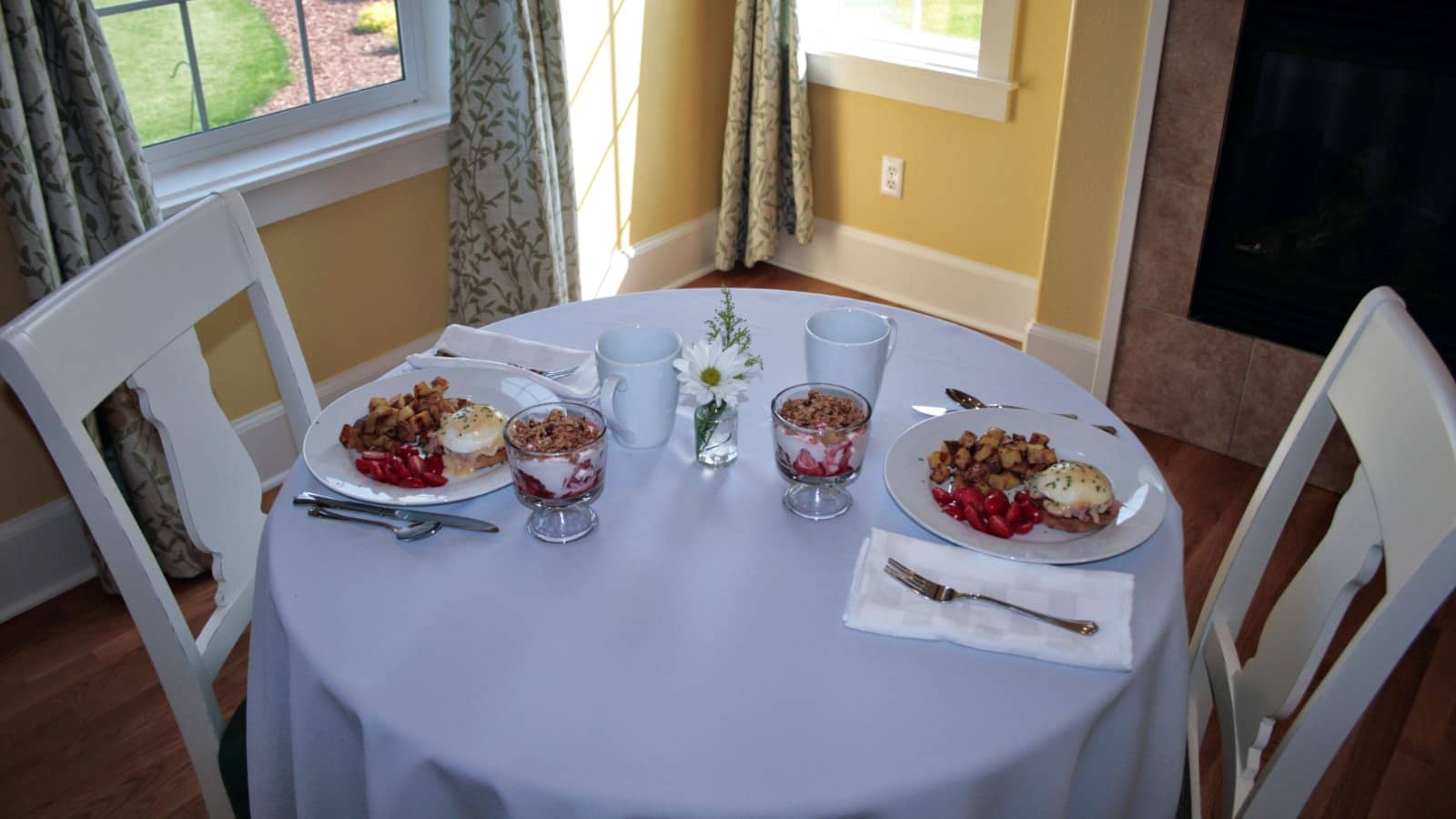 Round table with white tablecloth, two place settings each with a breakfast dish and fruit parfait