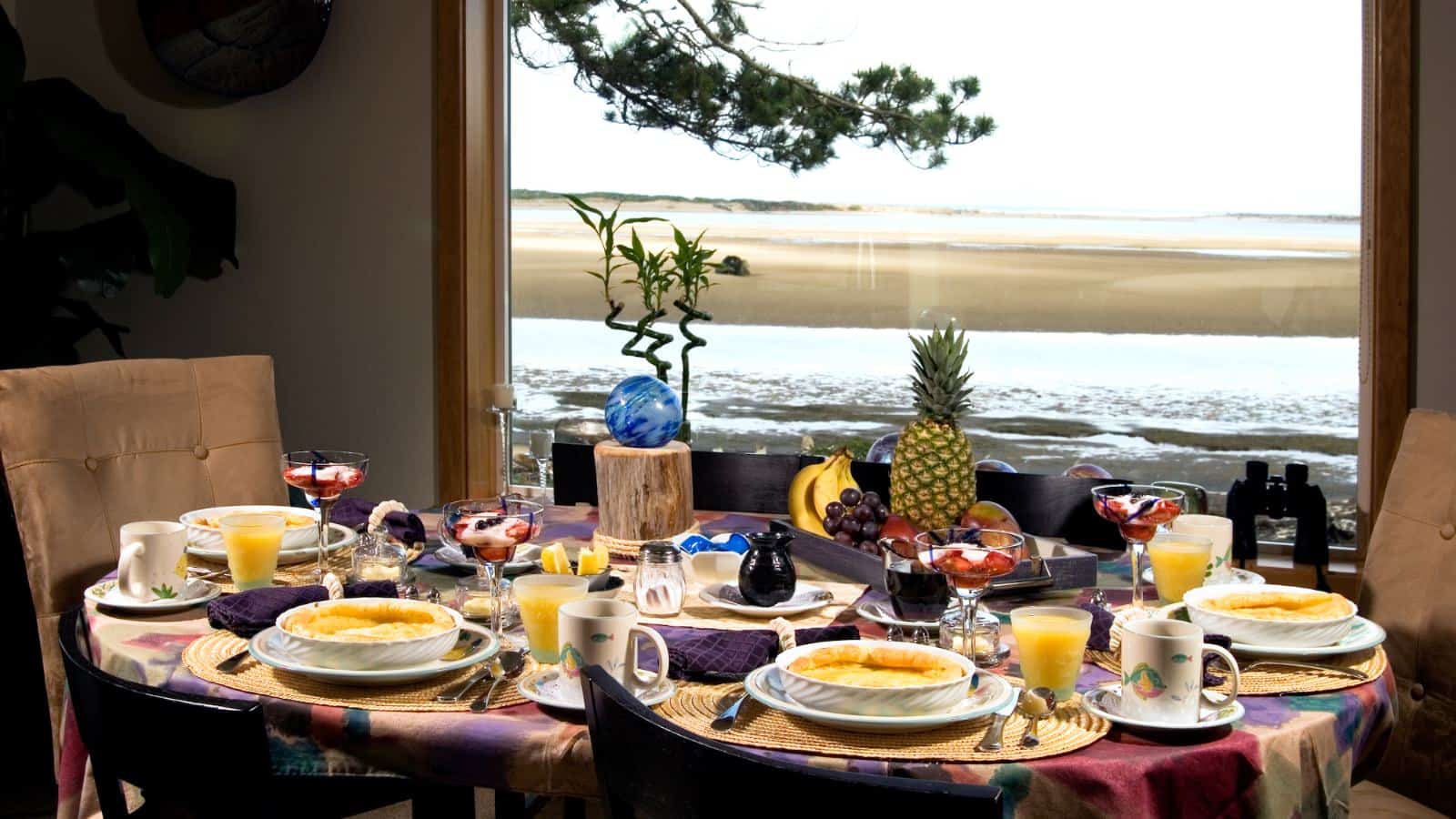 Dining table with five place settings with breakfast dishes and a large window with view of the beach