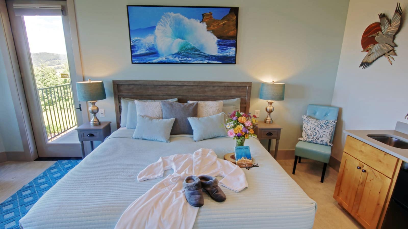 Bedroom with light green and white walls, hardwood flooring, light wooden headboard, light blue bedding, and vanity with sink