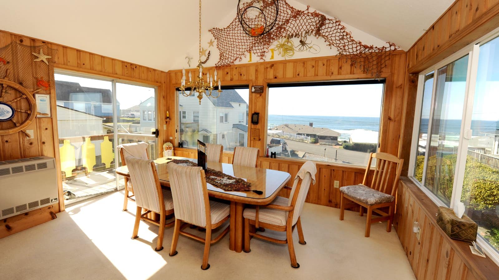 Large dining room with wooden table and wooden and upholstered chairs and large windows looking out over other houses and the water