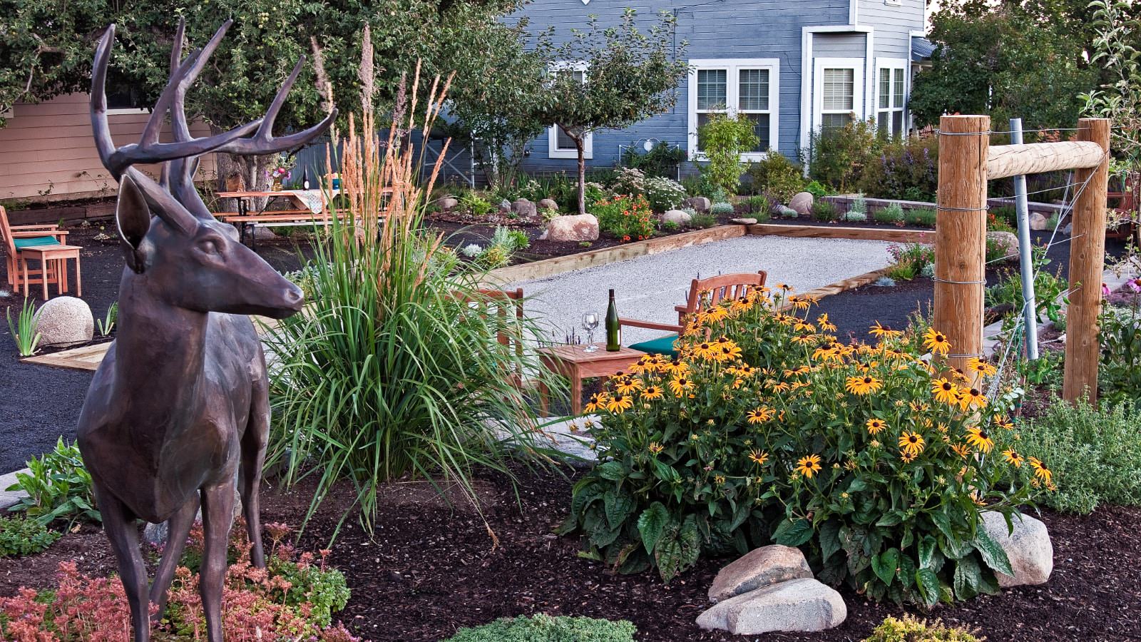 Large bronze sculpture of deer with antlers in a garden with bocce court surrounded by flowers, bushes, and trees