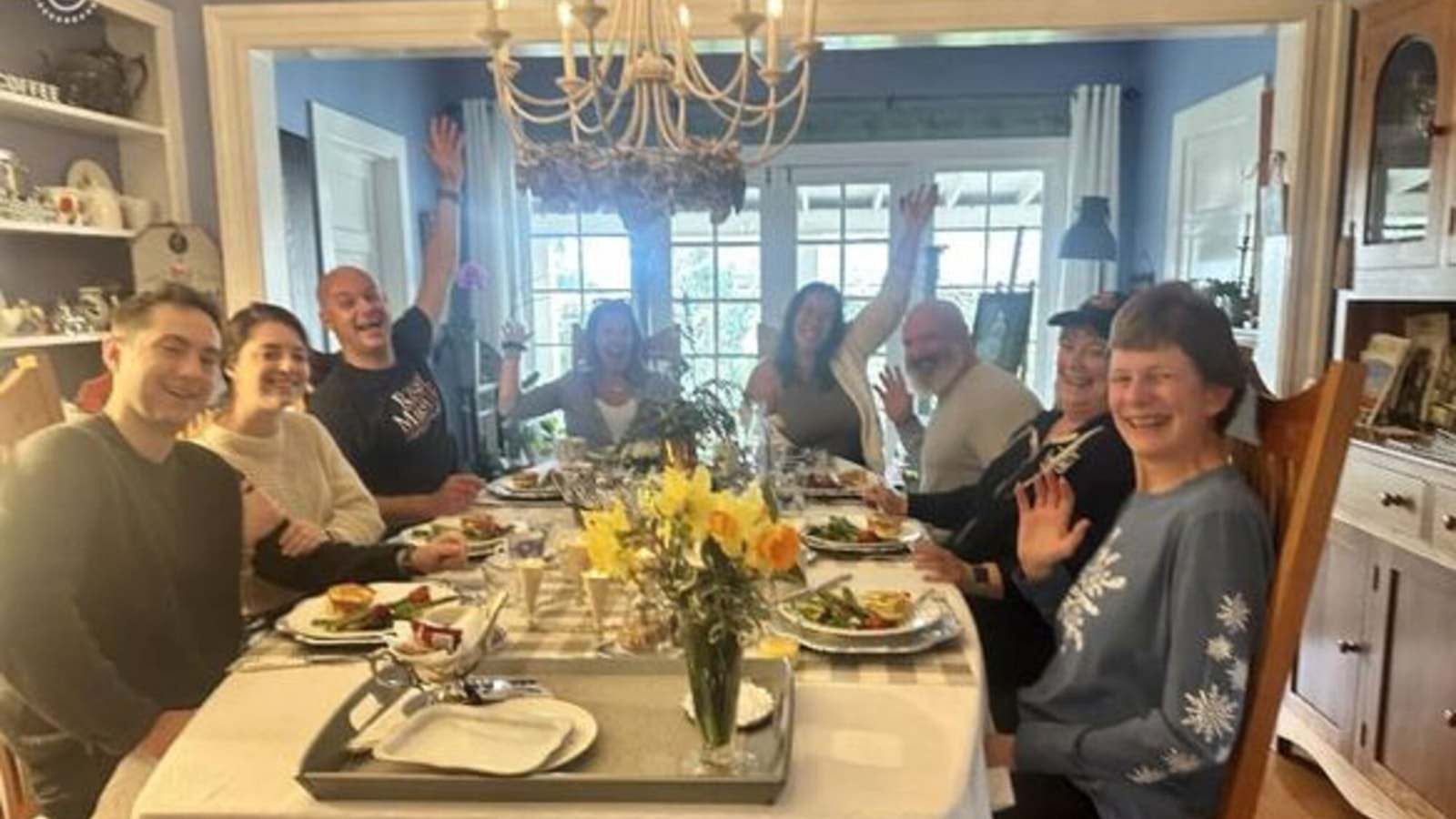 Dining room with multiple place settings with many people smiling and waving