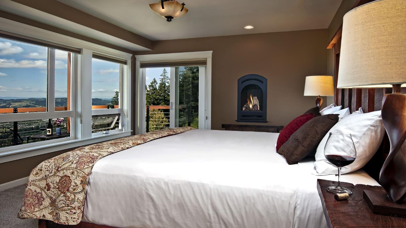 Bedroom with brown walls, white trim, carpeting, wooden bed, white bedding, and large windows with views of the area