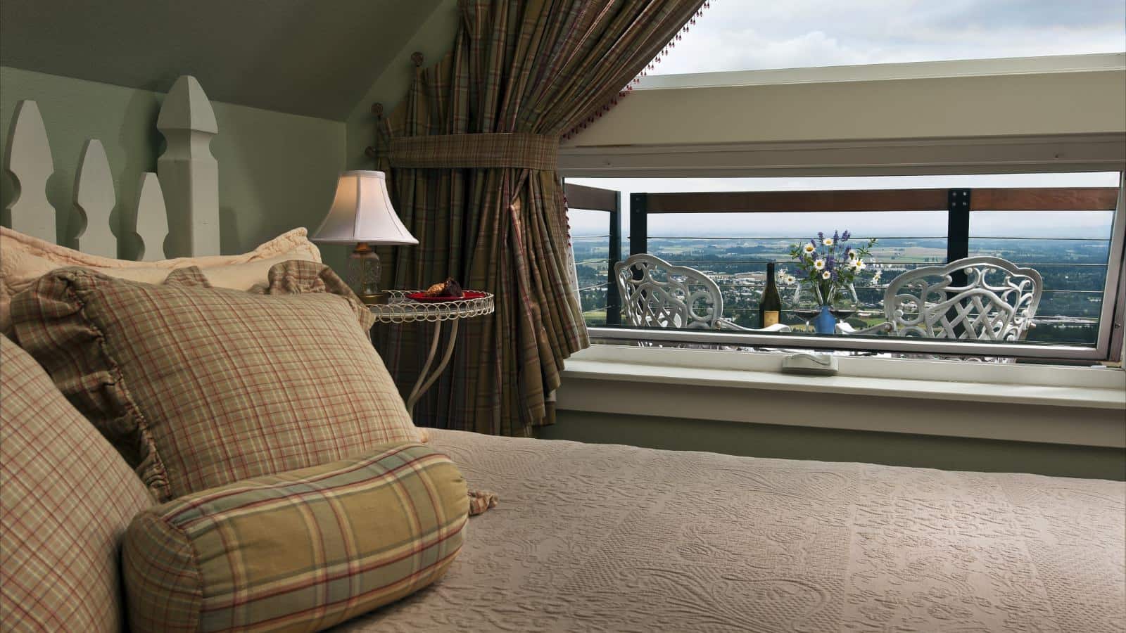 Bedroom with light green walls, white picket fence headboard, light-colored bedding, large window with views of the area