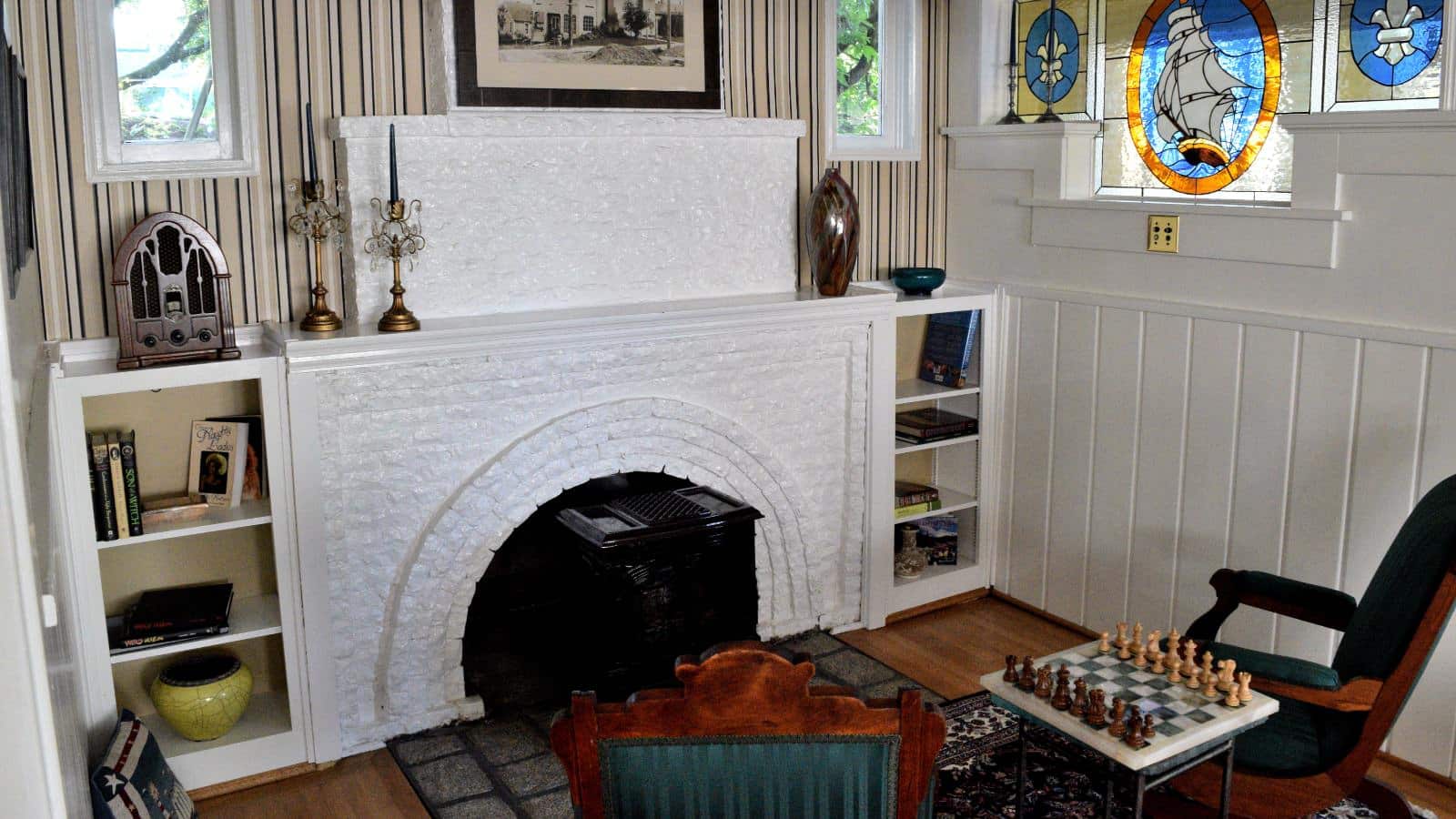 Living room with white painted brick fireplace, brown and green chairs, and chess set on small table between chairs