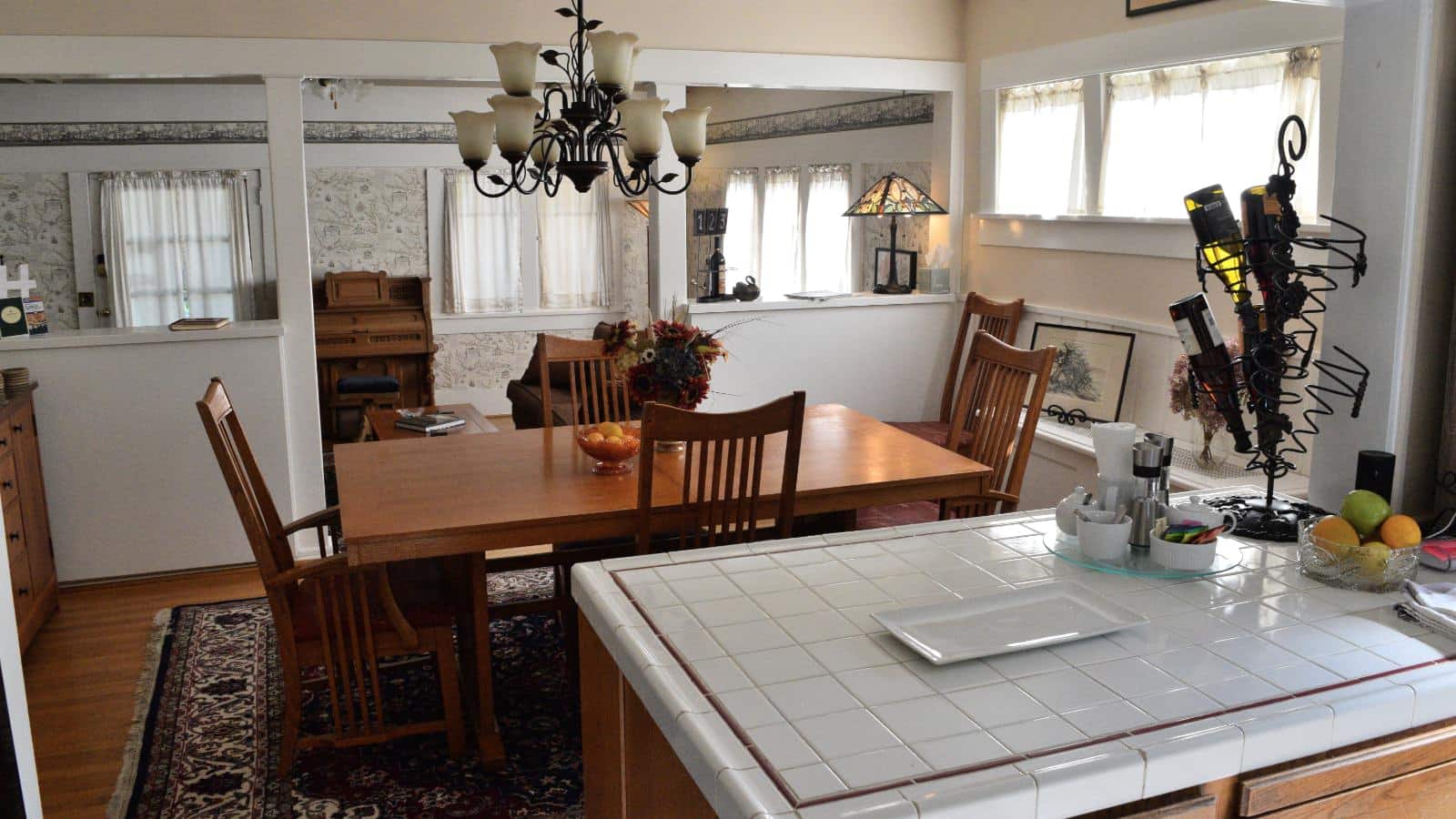 Kitchen with white tile countertops, wooden dining table with chairs, and view into living room