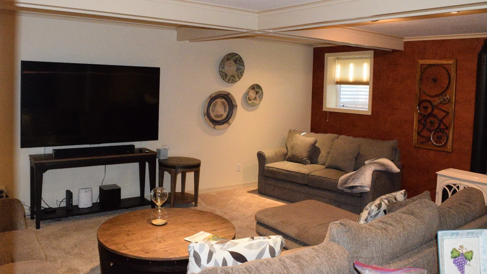 Living room with white and brown walls, carpeting, taupe upholstered sofa and love seats, and large flat-screen TV