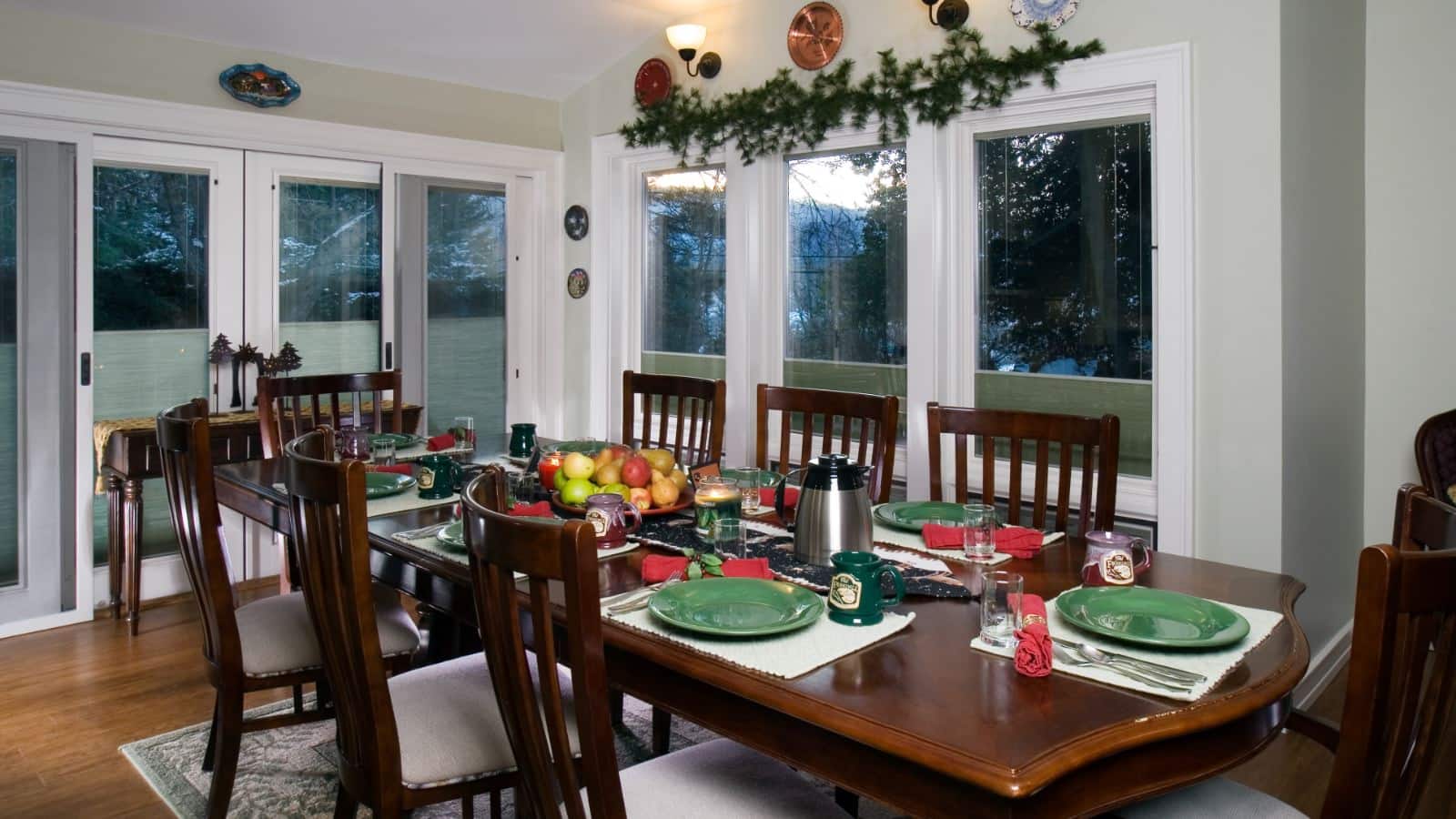 Dining room with long dark wooden table with multiple place settings, wooden chairs, and many windows with views of the outside