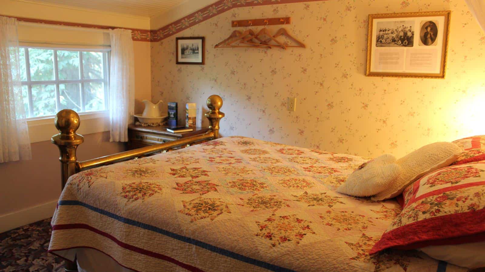 Bedroom with floral wallpaper, carpeting, multicolored bedding, and window with view of green trees