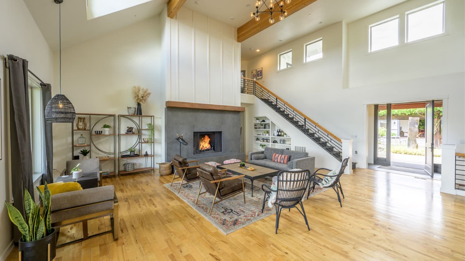 Large great room with white walls, hardwood flooring, vaulted ceiling, large fireplace, gray upholstered sofa, leather chairs, and gray metal chairs