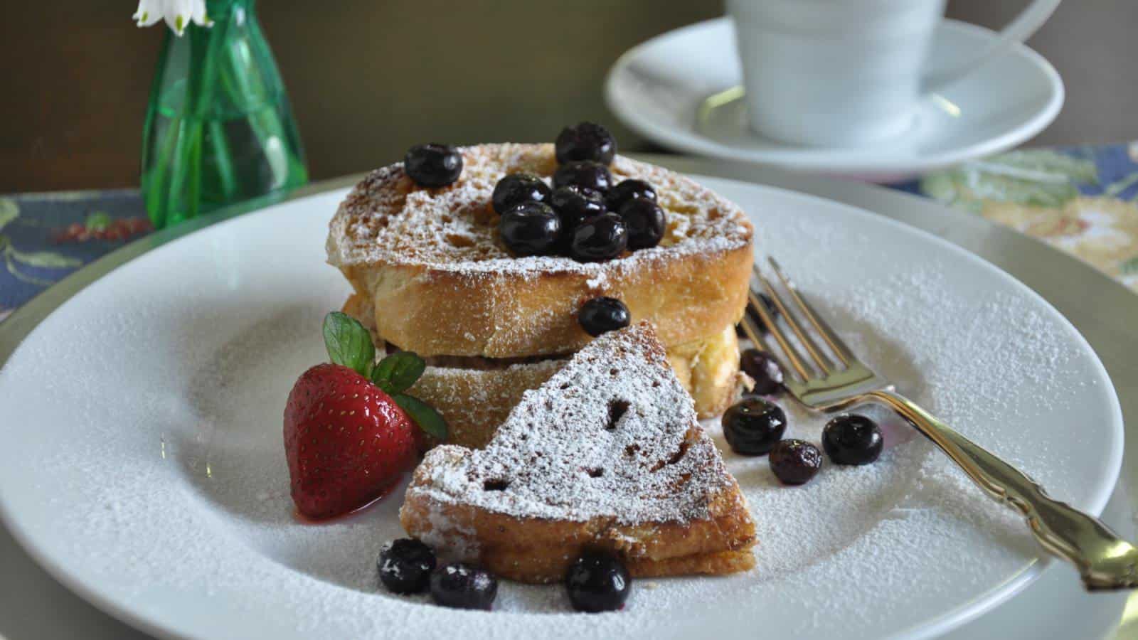 Close up view of white plate with french toast topped with blueberries and powdered sugar