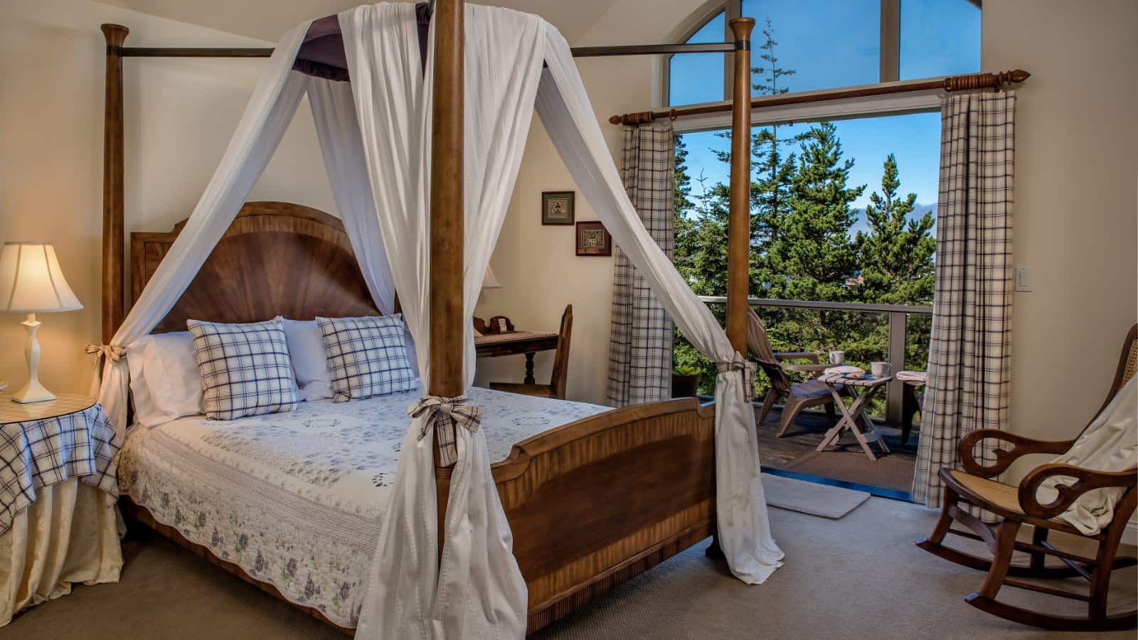 Bedroom with light colored walls, carpeting, wooden four poster bed with canopy, white bedding, and balcony with patio furniture
