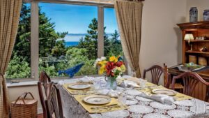 Dining room with wooden table and chairs, white tablecloth, place settings, and large window with views of the outside