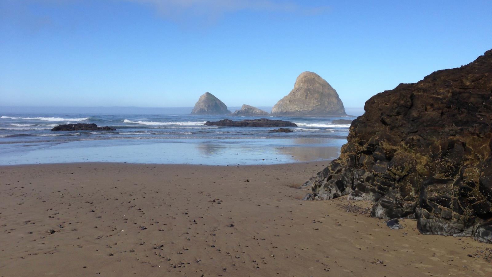 Wet sandy beach with soft rolling waves and three very large rocks in the protruding through the water