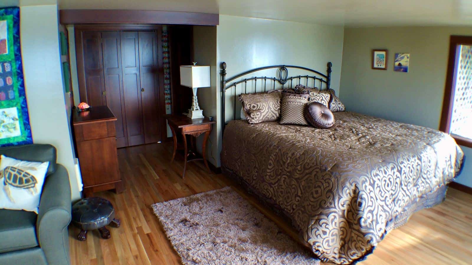 Bedroom with light green walls, hardwood flooring, wrought iron bed, brown bedding, wooden dresser, and green loveseat
