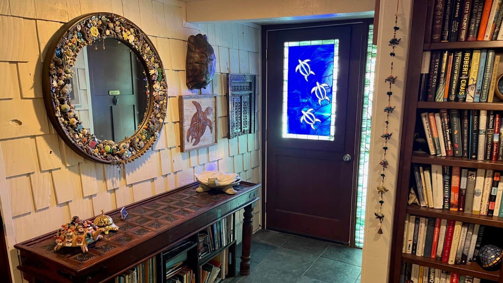 Foyer of property with light colored walls, green floor tiles, antique buffet table, bookshelf full of books, and large round mirror