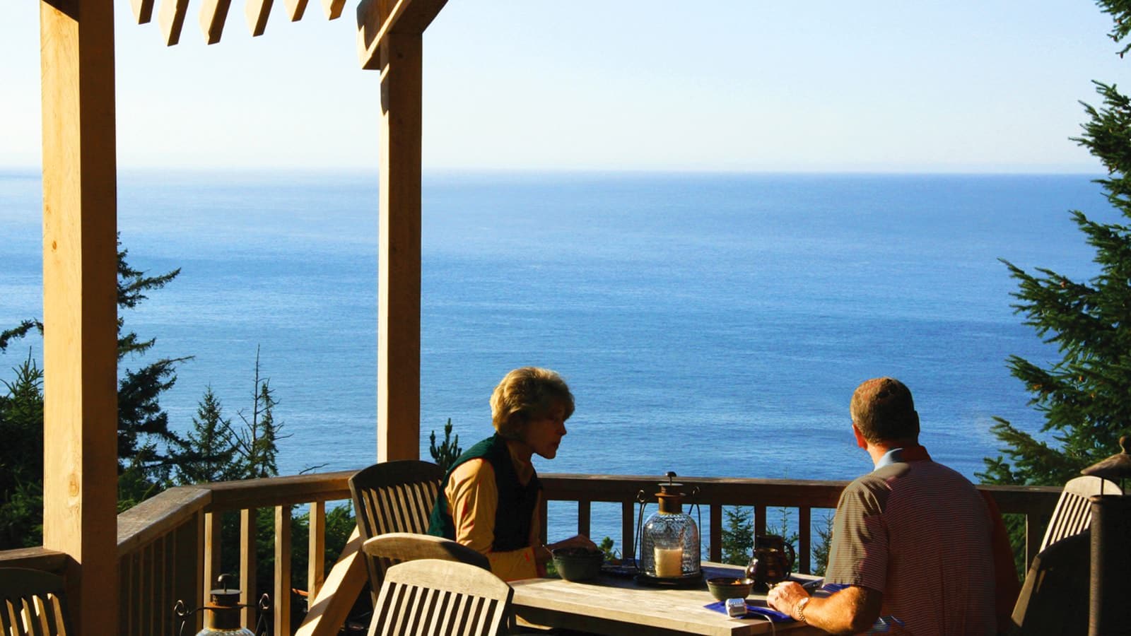 Man and woman sitting at wooden table overlooking the ocean in the background