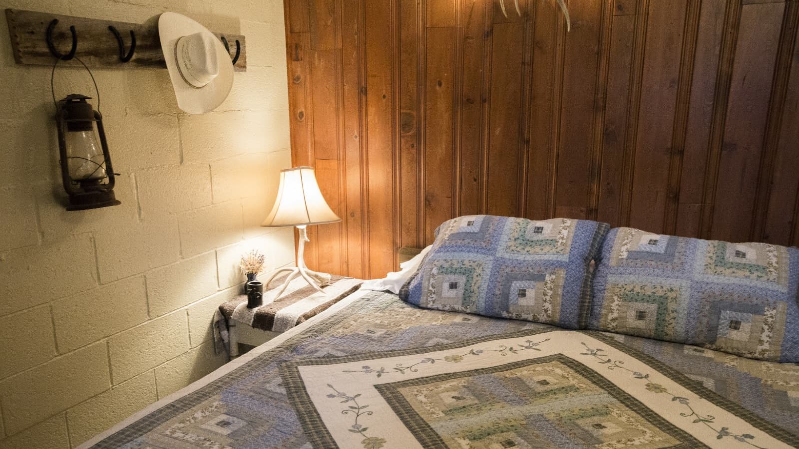Bedroom with painted cinder block and wood paneling on the walls, multicolored bedding, and hat rack made of wood and horseshoes