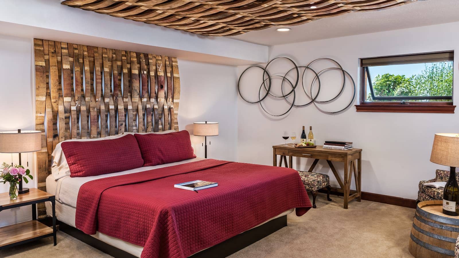 Bedroom with white walls, carpeting, custom wooden headboard, red bedding, wooden desk, and sitting area