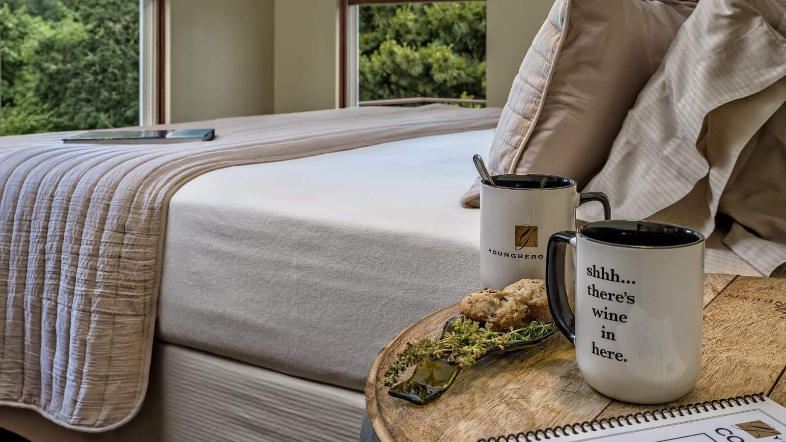 Close up view of coffee cups sitting on nightstand next to bed with light colored bedding