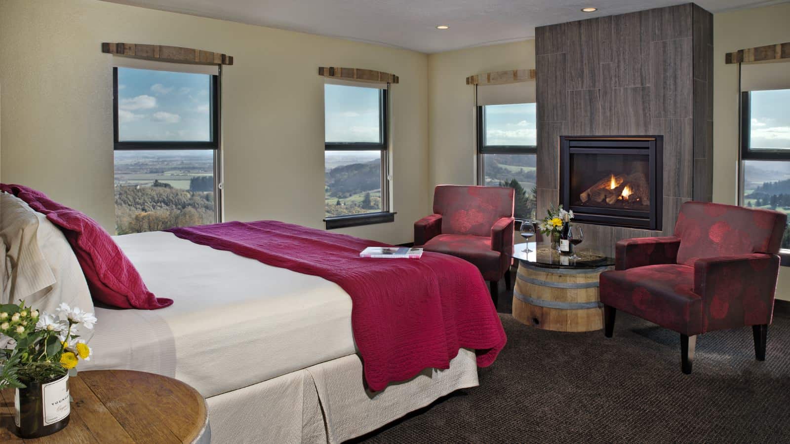 Bedroom with light colored walls, carpeting, large fireplace, white and red bedding, and sitting area with red armchairs