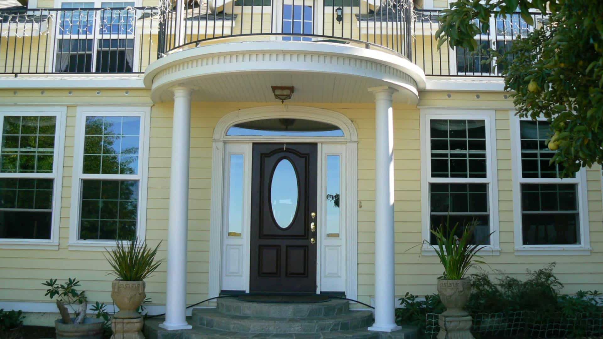 Exterior view of property painted yellow with white trim surrounded by green plants and trees