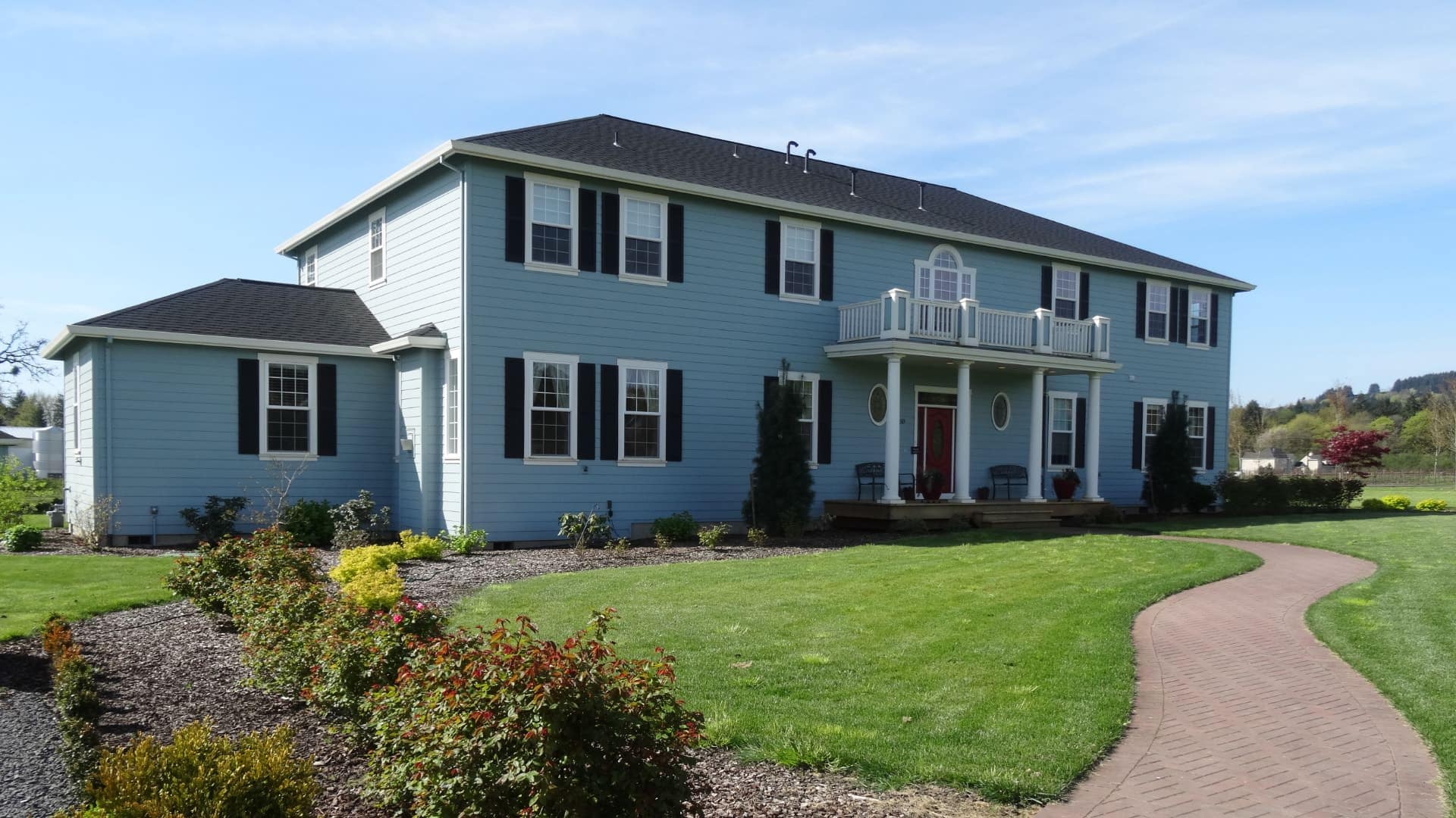 Exterior view of the property painted light blue with white trim and dark shutters surrounded by green grass, bushes and shrubs