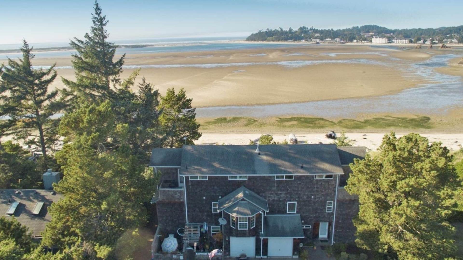 Aerial view of property surrounded by green trees and located near a beach and water