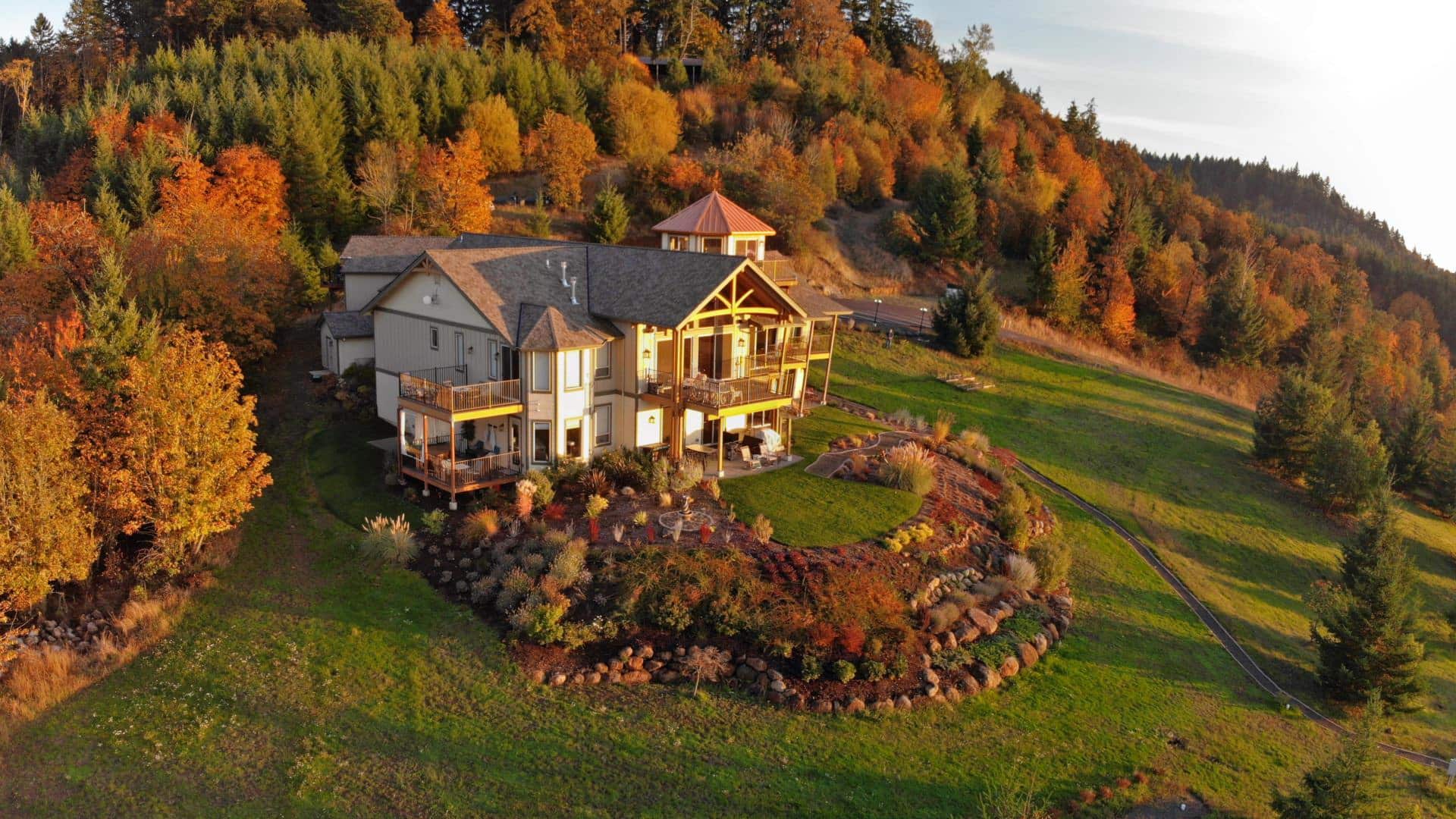 Aerial view of property surrounded by large green lawns, multicolored shrubs, and trees full of fall color