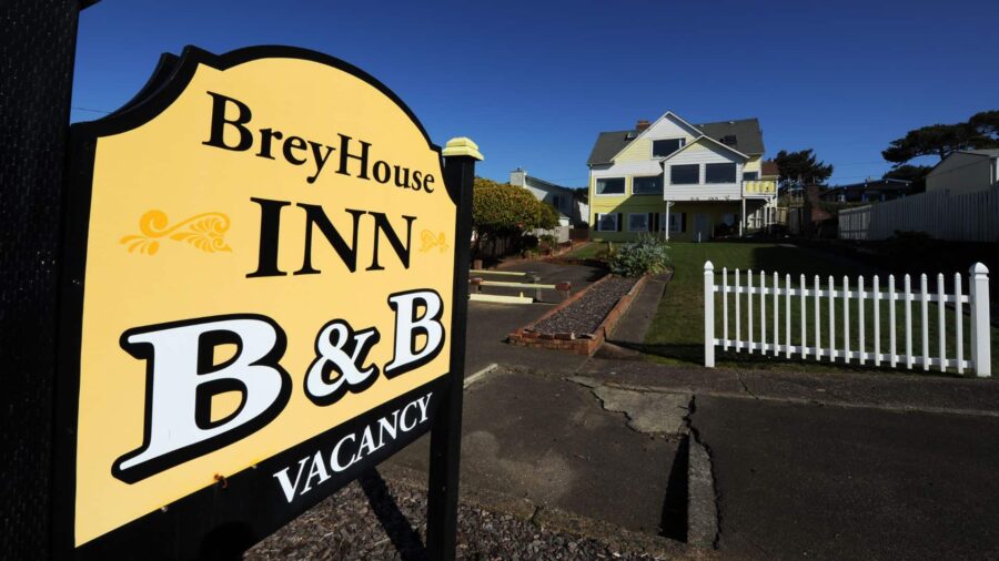 Exterior view of the property painted yellow with white trim, green lawn, white picket fence, and large BreyHouse Inn B&B sign