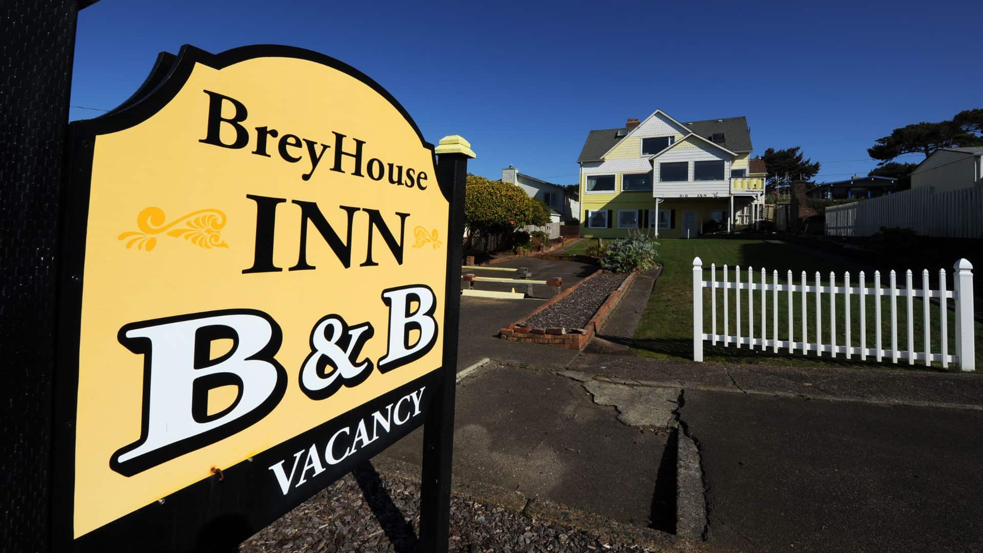 Exterior view of the property painted yellow with white trim, green lawn, white picket fence, and large BreyHouse Inn B&B sign