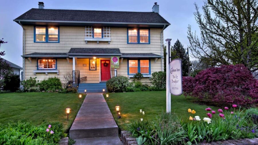 Exterior view of property painted cream with blue trim surrounded by green grass, bushes, shrubs, and flowers