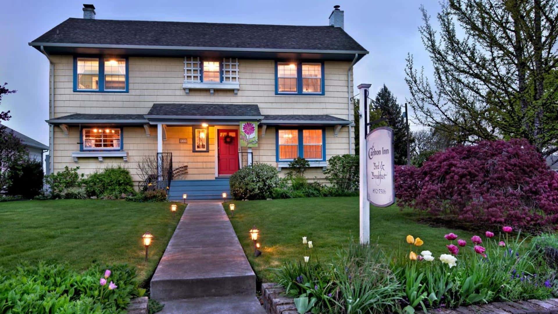 Exterior view of property painted cream with blue trim surrounded by green grass, bushes, shrubs, and flowers