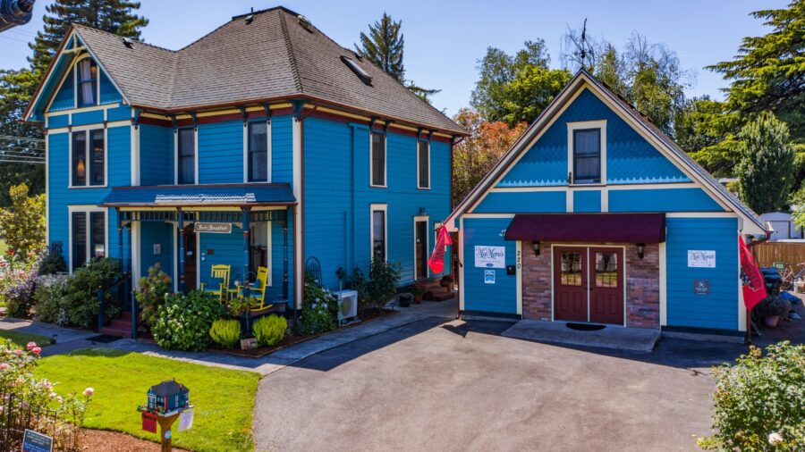 Exterior view of property painted blue with white trim surrounded by lush bushes, flowers, and green trees