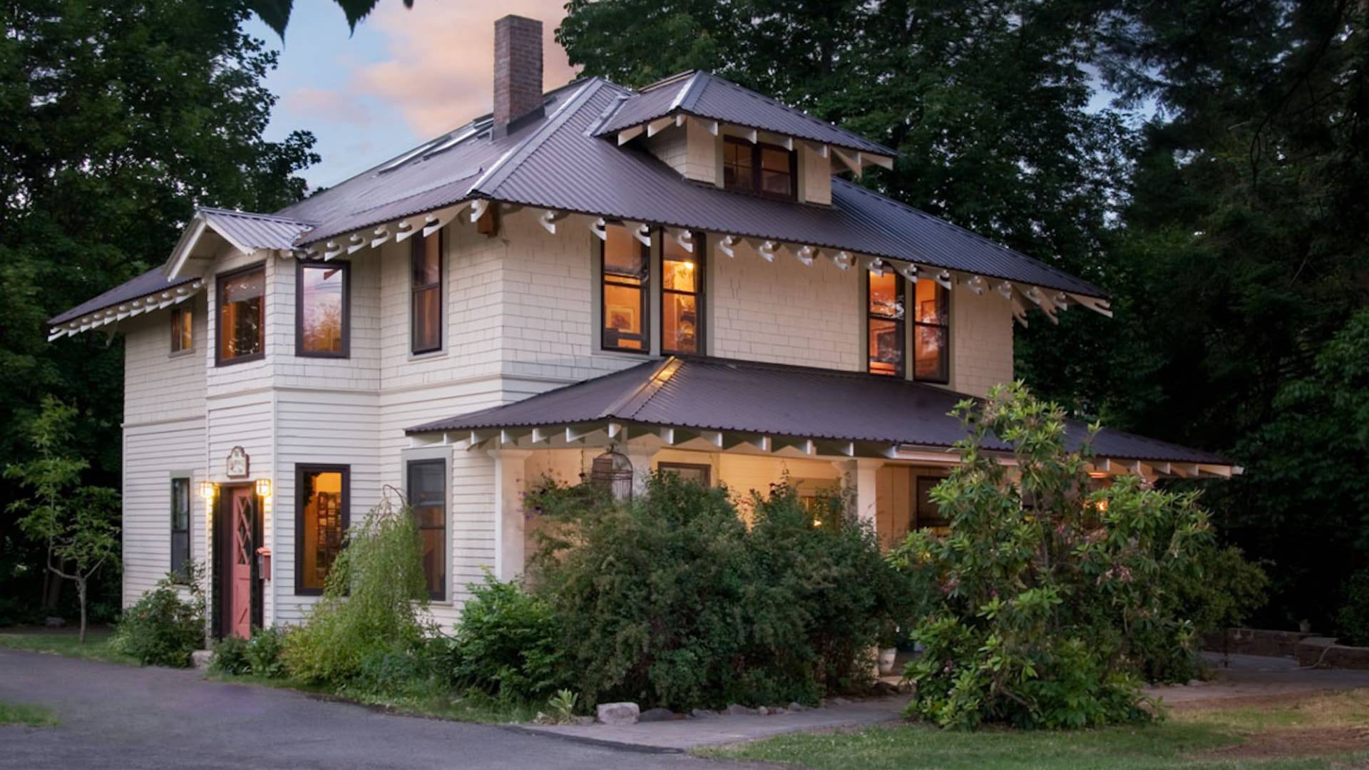 Exterior view of property painted cream with light gray trim surrounded by lush bushes and trees