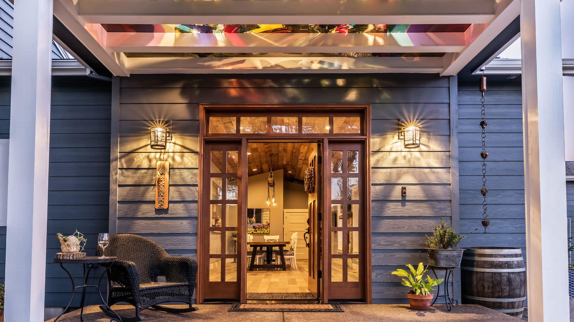 Close up view of properties entrance with wooden front door surrounded by multiple glass panes, wicker patio chair, and small metal table