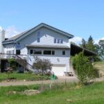 Exterior view of property painted light blue with white trim surrounded by green grass, trees, shrubs, and flowers