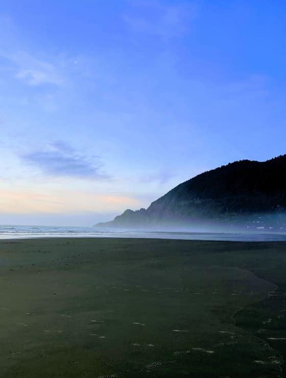 Large wet beach with soft rolling waves with large rocky hill next to the water