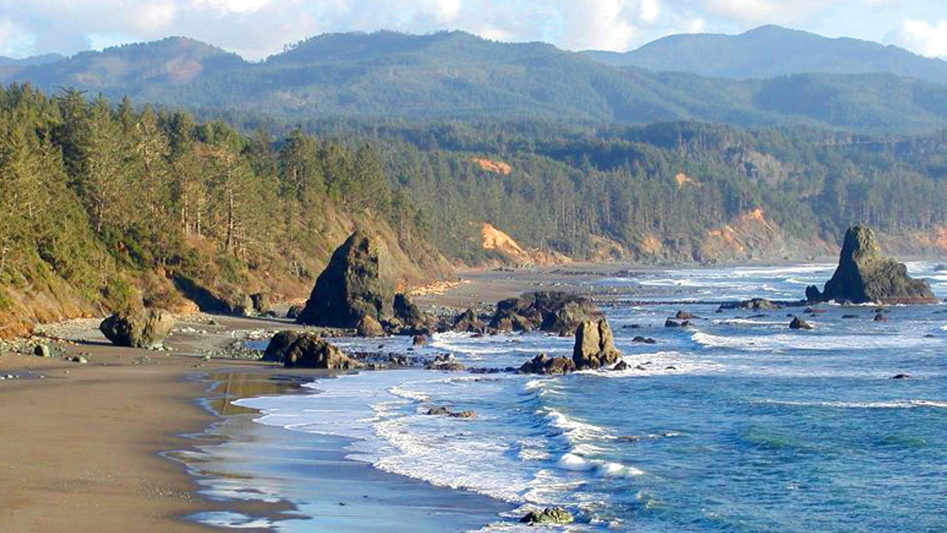 Mountain range next to ocean with soft waves hitting the beach