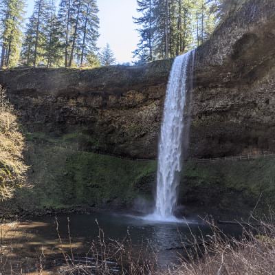 Small waterfall coming off the top of a large rock formation surrounded by green trees